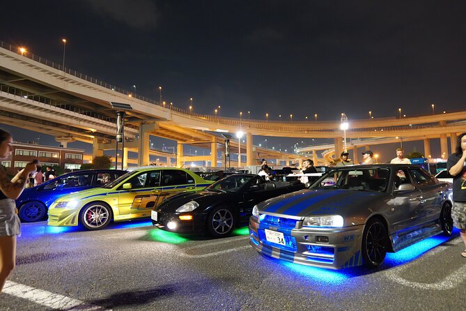 Tuned JDM cars with neon underglow lined up at night under the Daikoku PA expressway junction
