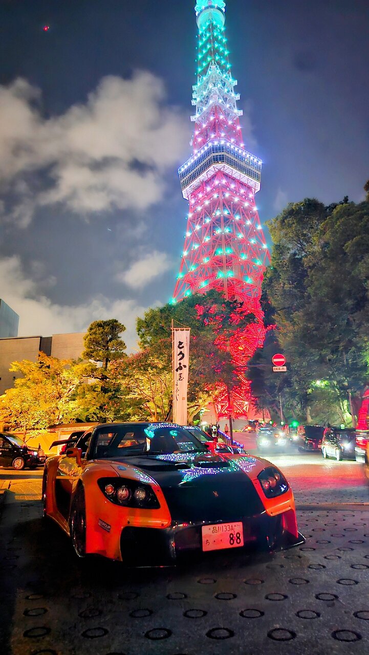 Veilside RX-7 decorated with lights parked in front of illuminated Tokyo Tower at night